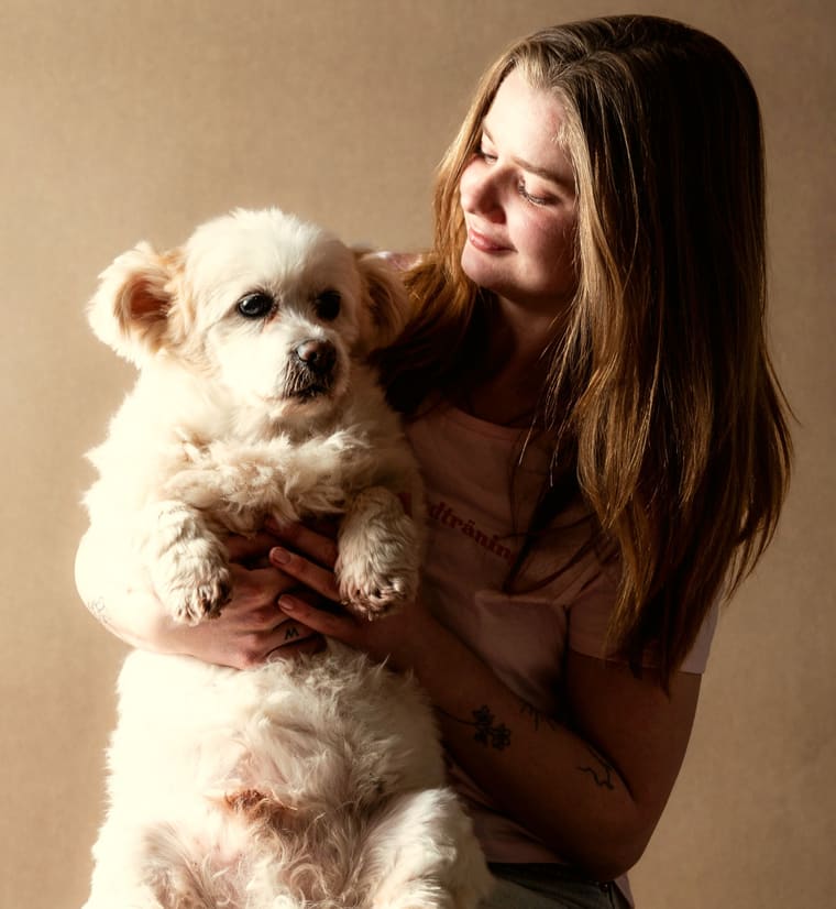 Ulrika Winge håller upp en vit, lurvig hund och ler mot den