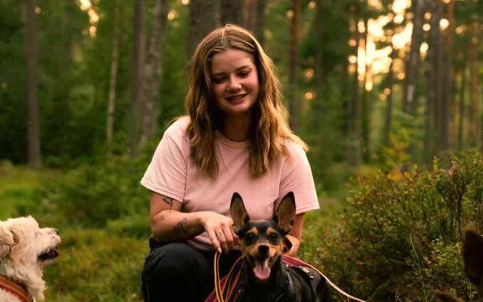 Ulrika Winge sitter på huk på en skogsstig med en liten hund i koppel